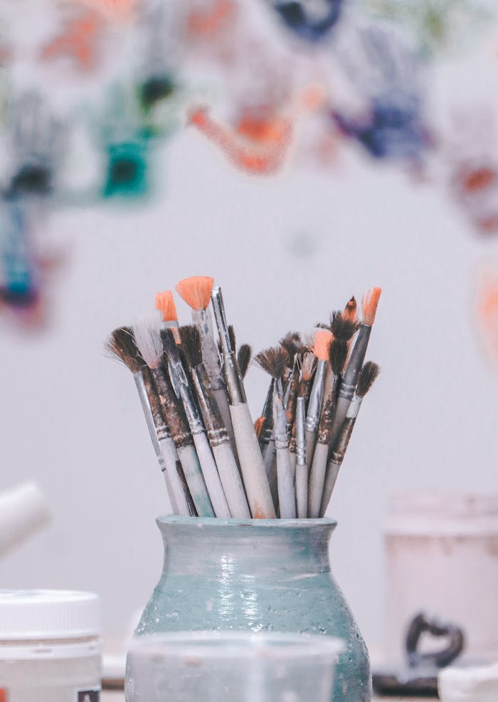A vibrant collection of paintbrushes in a ceramic vase with blurred colorful art in the background.